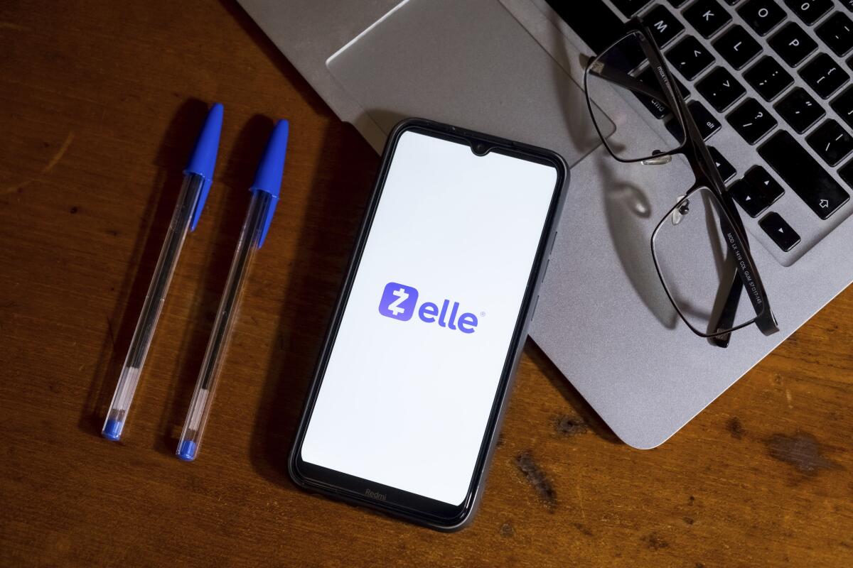 A Zelle logo is seen on a smartphone next to a laptop.