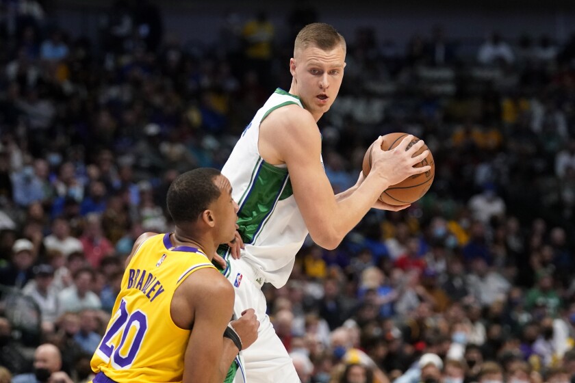 Los Angeles Lakers guard Avery Bradley (20) as Dallas Mavericks center Kristaps Porzingis, right, looks for an opening to the basket in the first half of an NBA basketball game in Dallas, Wednesday, Dec. 15, 2021. (AP Photo/Tony Gutierrez)
