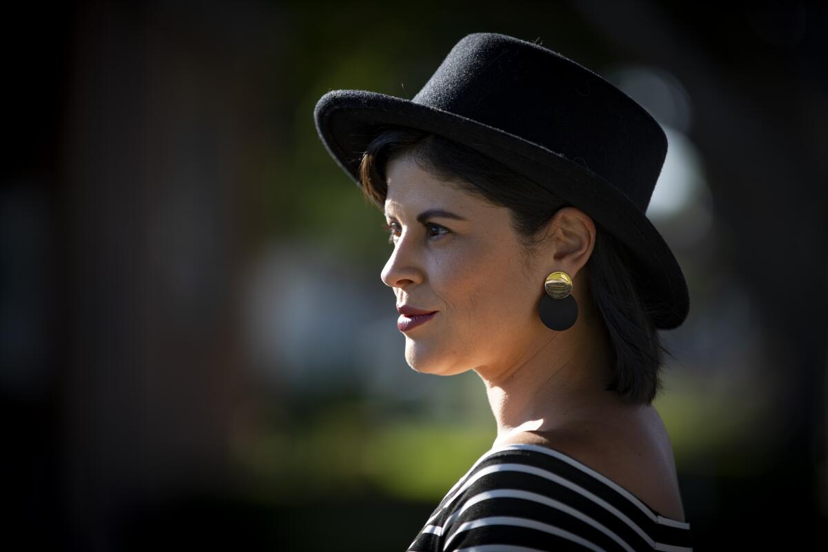 TV writer Judalina Neira poses in a black hat, black and white striped top, and black and gold earrings.