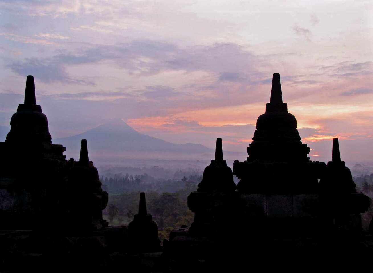 Mt. Merapi rises in the distance behind the stupas at Borobudur, a majestic, ancient temple devoted to Buddha in Indonesia. The temple is one of three great religious sites in Southeast Asia, but it's older and more esoteric than Bagan in Myanmar and Angkor Wat in Cambodia.