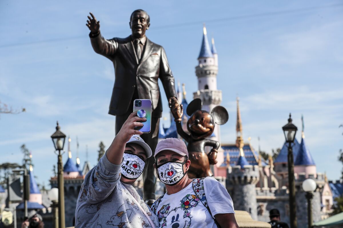 Masked visitors take a selfie in front of a statue of Walt Disney and Mickey Mouse inside Disneyland.