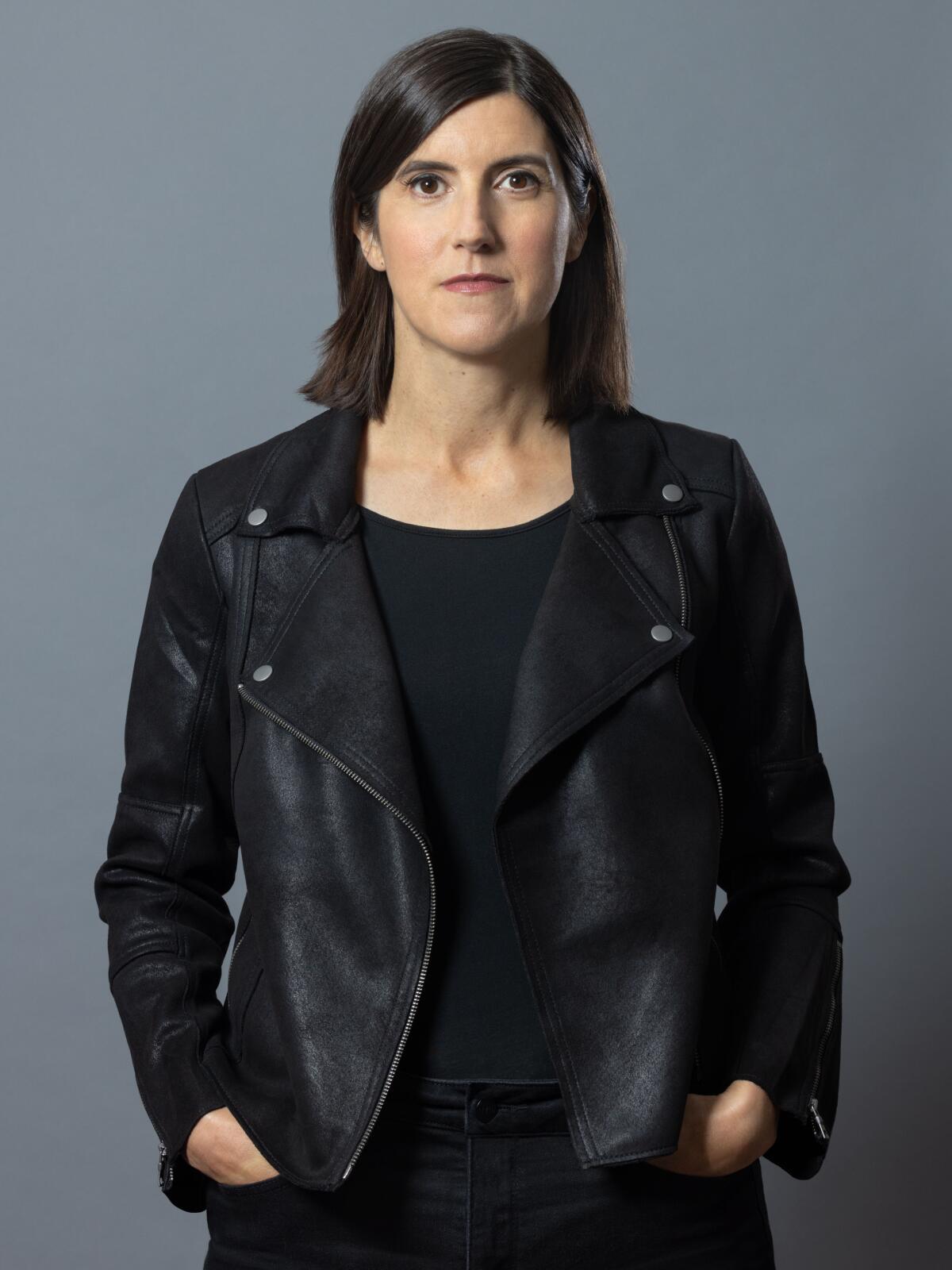 A writer with dark hair wears a black shirt and leather jacket against a gray background.