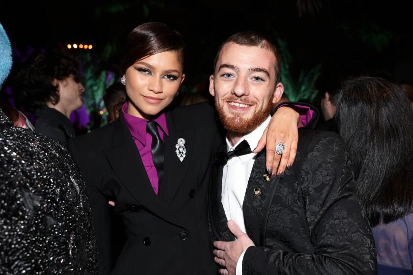 Zendaya wearing a black and purple suit embracing and posing with Angus Cloud in a black tuxedo