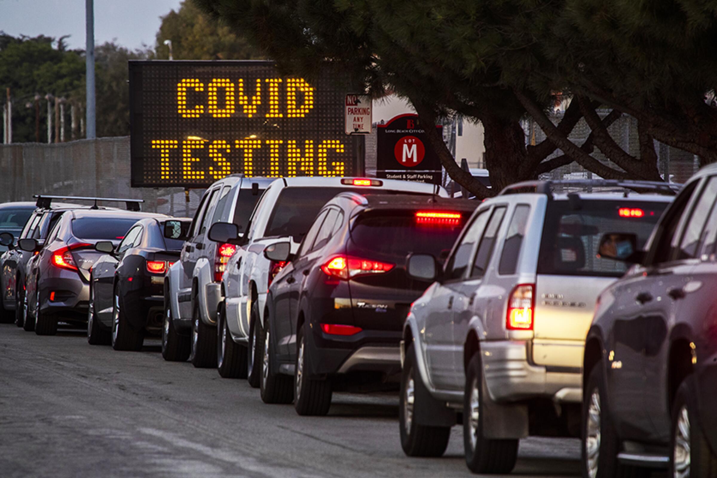 A line of cars near an electronic sign that says, "COVID testing."