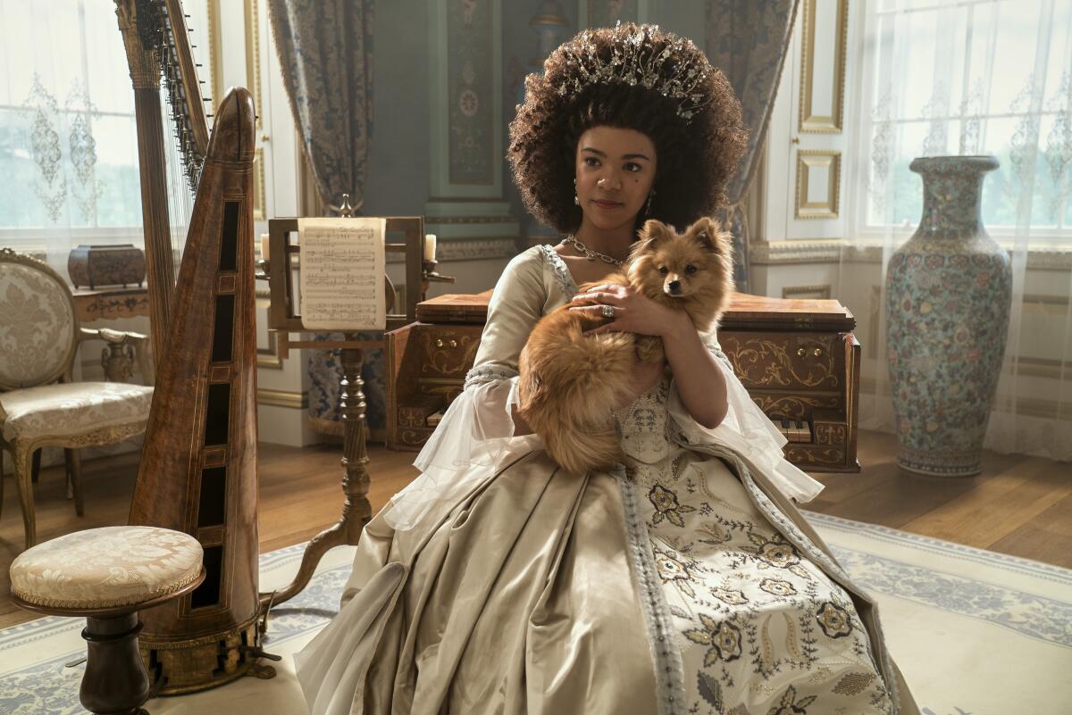 A queen sits in a parlor holding a small brown dog in her arms.