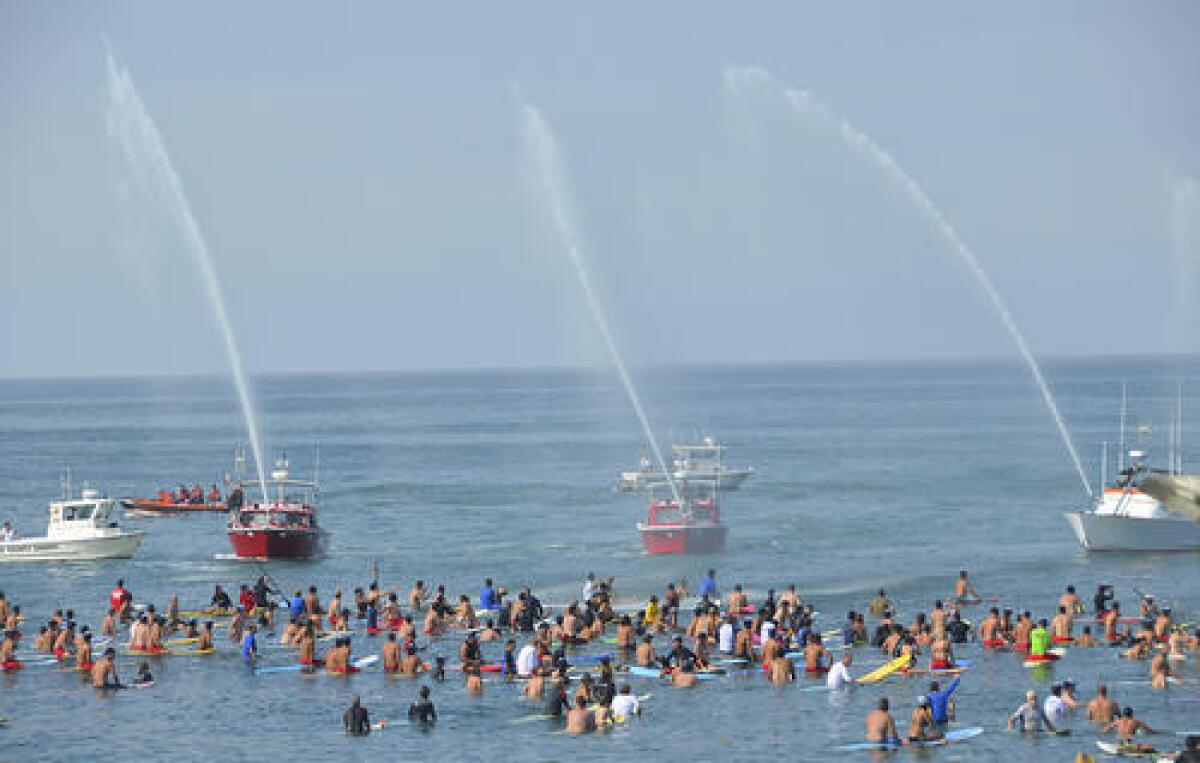 Three lifeguard rescue boats from neighboring agencies shoot their water cannons into the sky during memorial paddle out service for Newport Beach lifeguard Ben Carlson at the Newport Pier on Sunday.