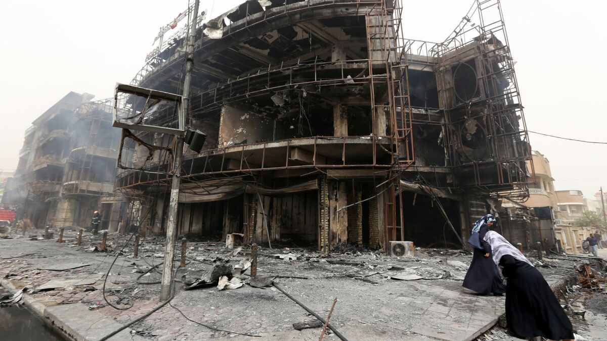 Iraqi women walk past a damaged building at the site of a suicide car bombing in Baghdad's central Karada district.