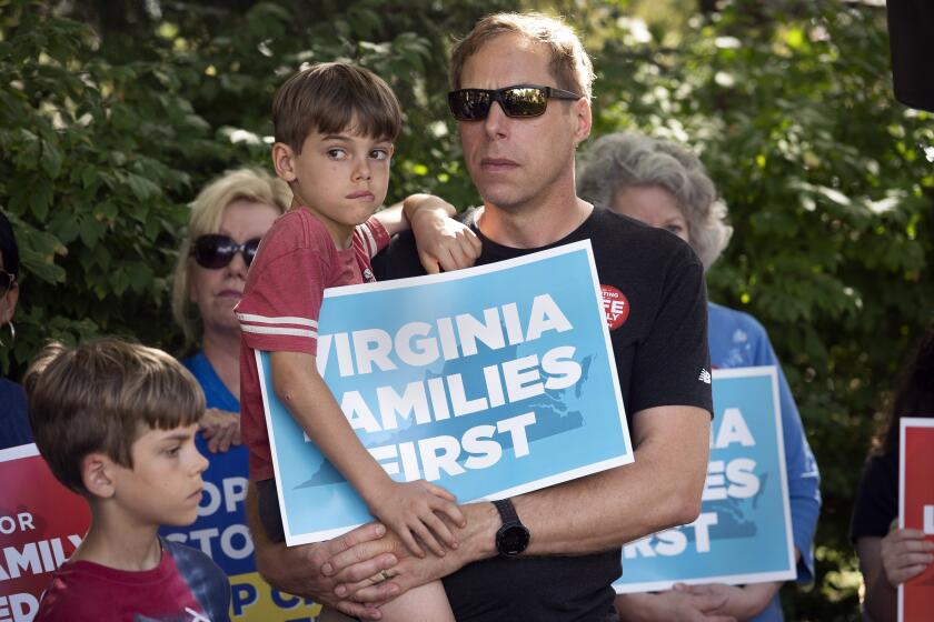 Patrick Novecosky, of Warrenton, Va., holds his son Daniel, 7, and son Peter, 9 stands beside them, as they participate in a rally sponsored by Catholic Vote and Fight for Schools, in Leesburg, Va., Saturday, Oct. 2, 2021. When Democrat Terry McAuliffe said during the Virginia governor’s debate last week that he doesn’t believe “parents should be telling schools what they should teach,” his opponent pounced. Republican Glenn Youngkin quickly turned the footage into a digital ad, then announced spending $1 million on a commercial airing statewide proclaiming that “Terry went on the attack against parents.” (AP Photo/Cliff Owen)