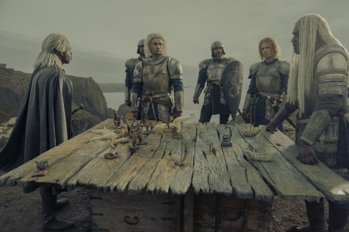 A group of men in armor stand around a table overlooking the coastline.