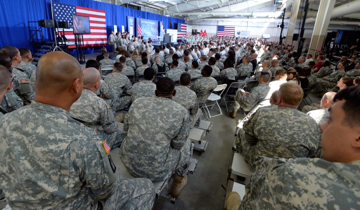 Military servicemembers sit in chairs and listen to speakers