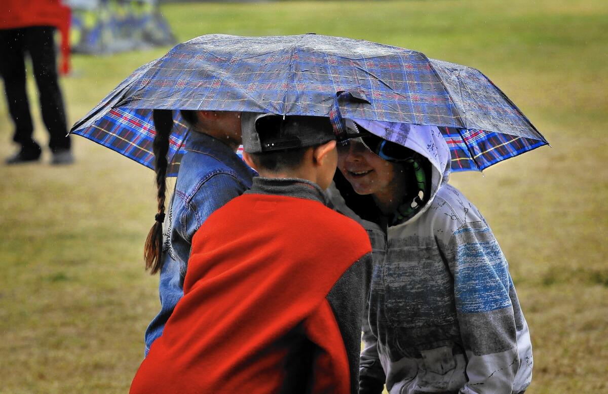 Children huddle beneath an umbrella as rain begins to fall on an evacuation camp for fire victims at the Napa Valley Fairgrounds in Calistoga, Calif.