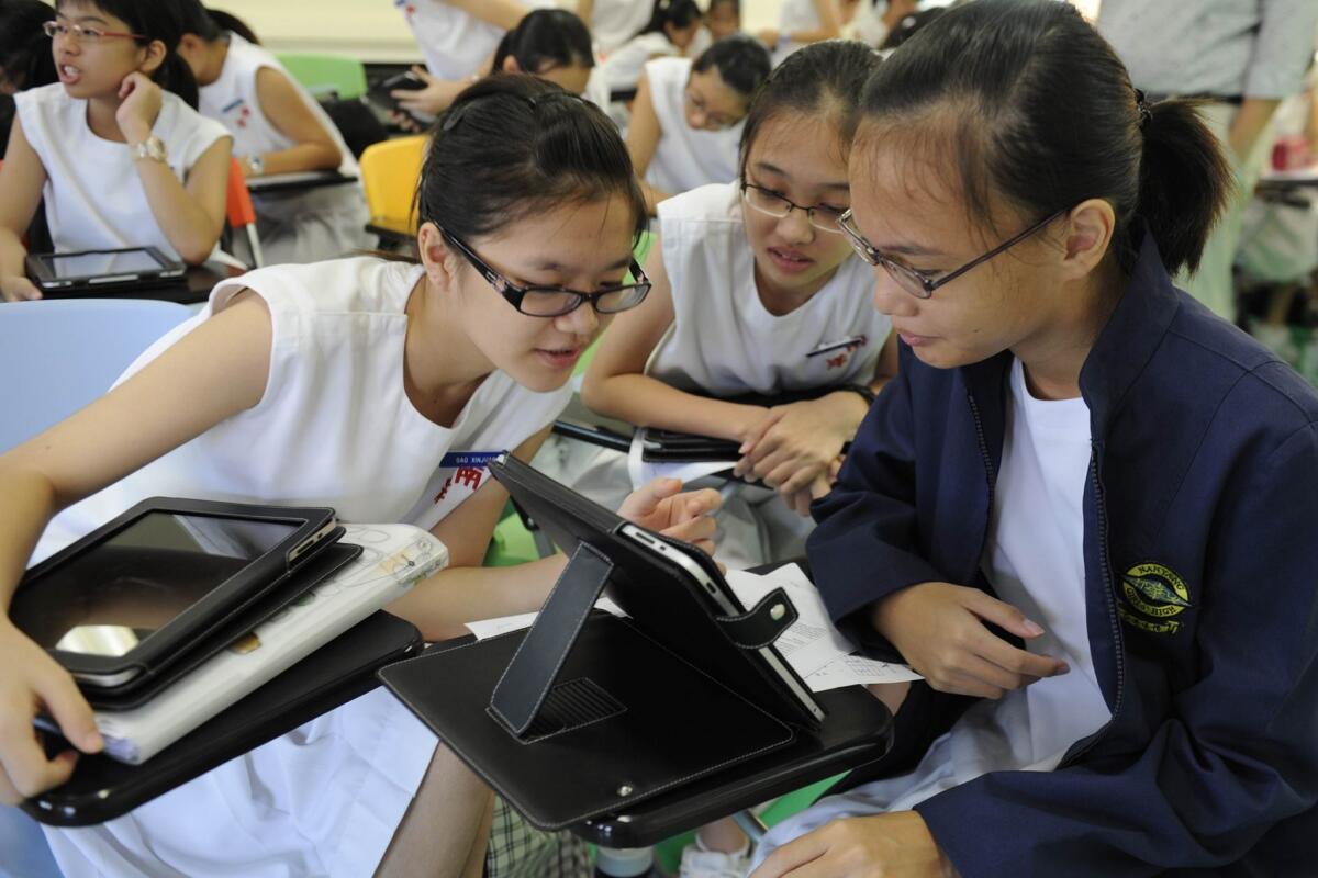 High school girls in Singapore look at information on a tablet. Singapore is among the nations whose students lead in reading.