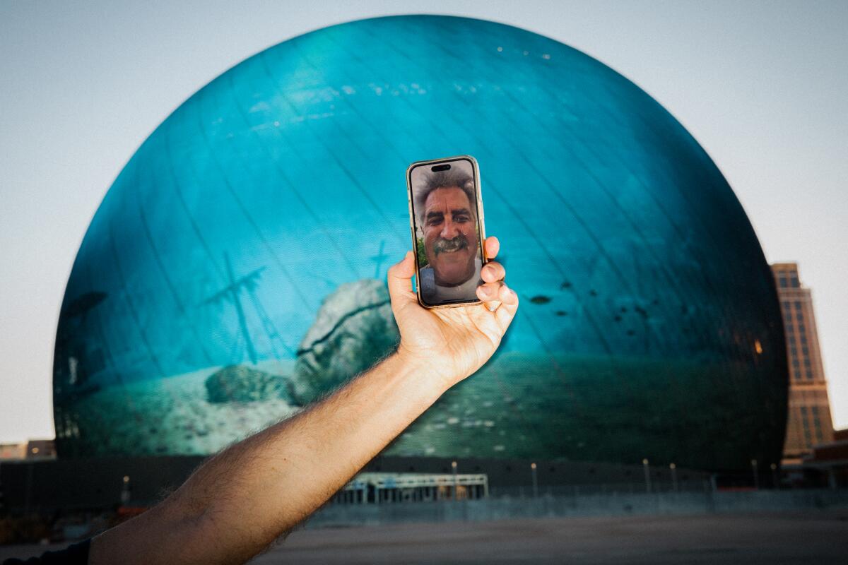 A man takes a Facetime call while standing in front of a spherical building that is illuminated to resemble an ocean