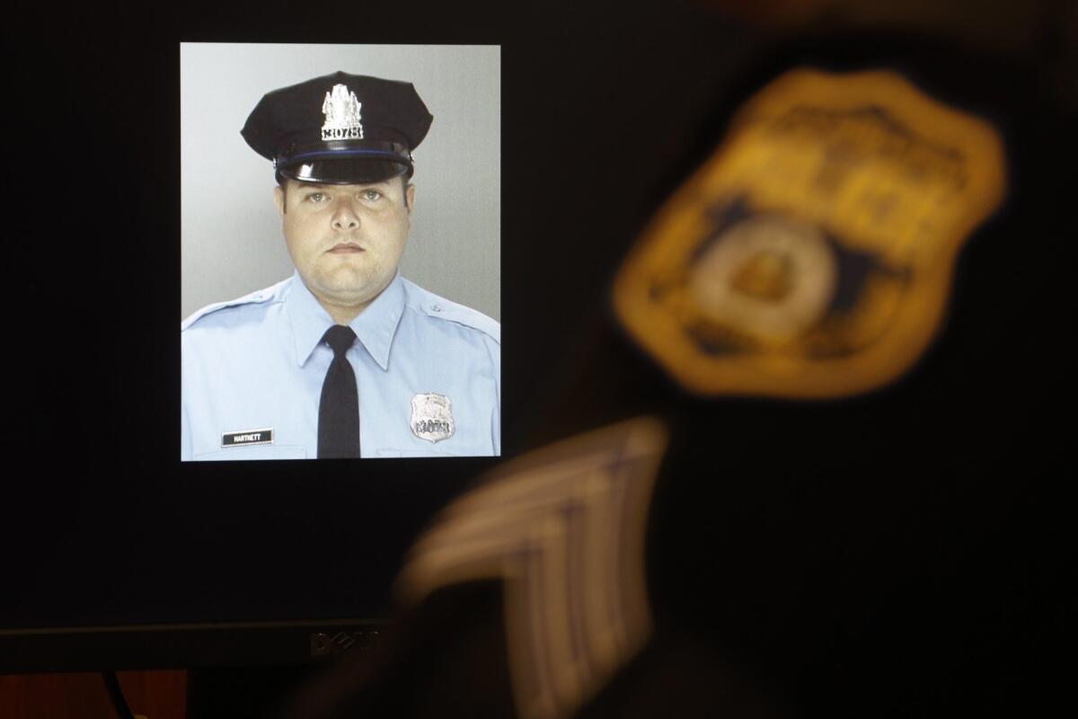 An officer sits next to a displayed image of Officer Jessie Hartnett before a news conference in Philadelphia on Friday. Hartnett is expected to survive the Thursday night attack.