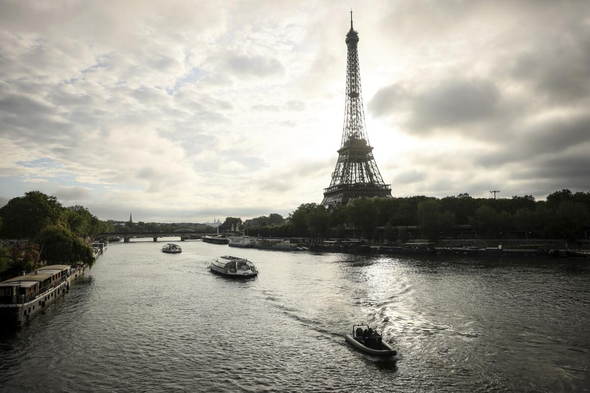 Barges cruise on the Seine river near the Eiffel Tower under a mostly cloudy sky