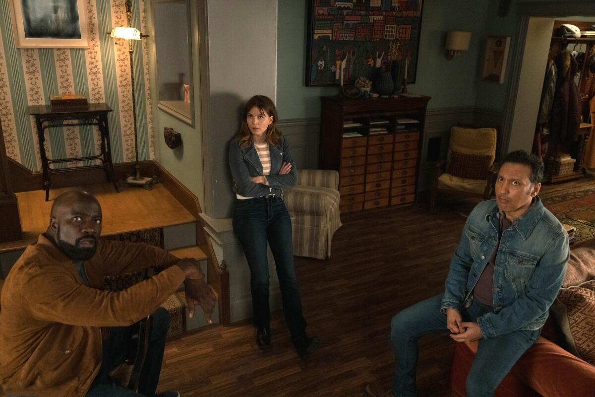 A man, a woman and another man wait in a living room.