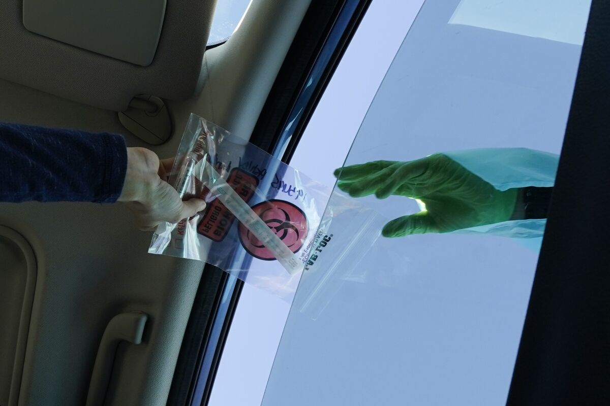 A COVID-19 test is handed through the vehicle window at a mobile testing site on Tuesday, Dec. 1, 2020, in Long Beach, Calif. (AP Photo/Ashley Landis)