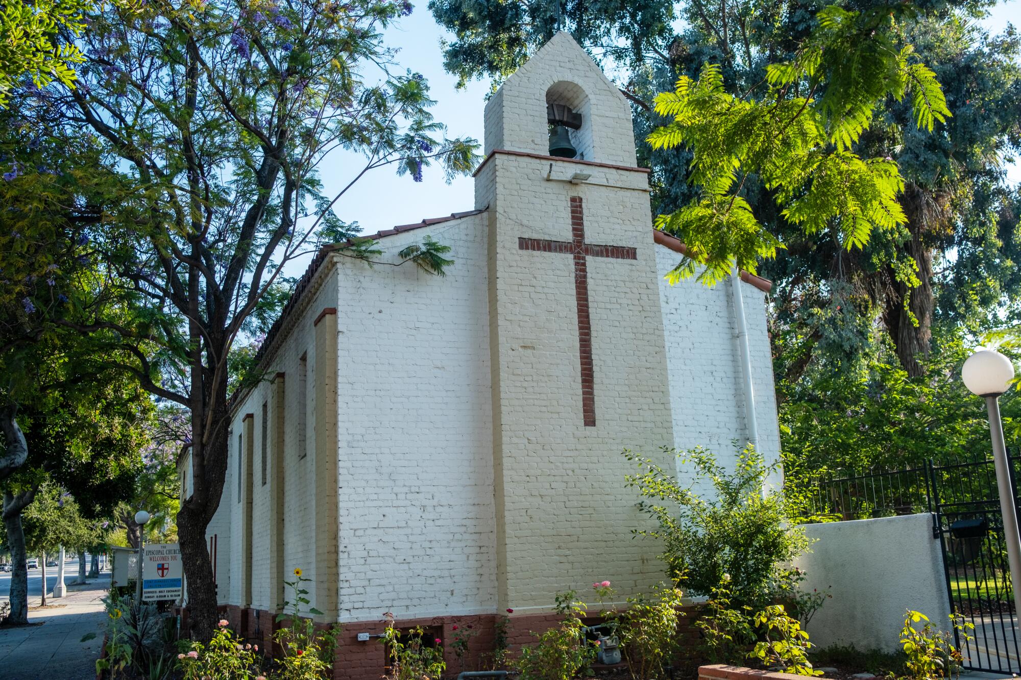 A white church is framed by leafy green trees.