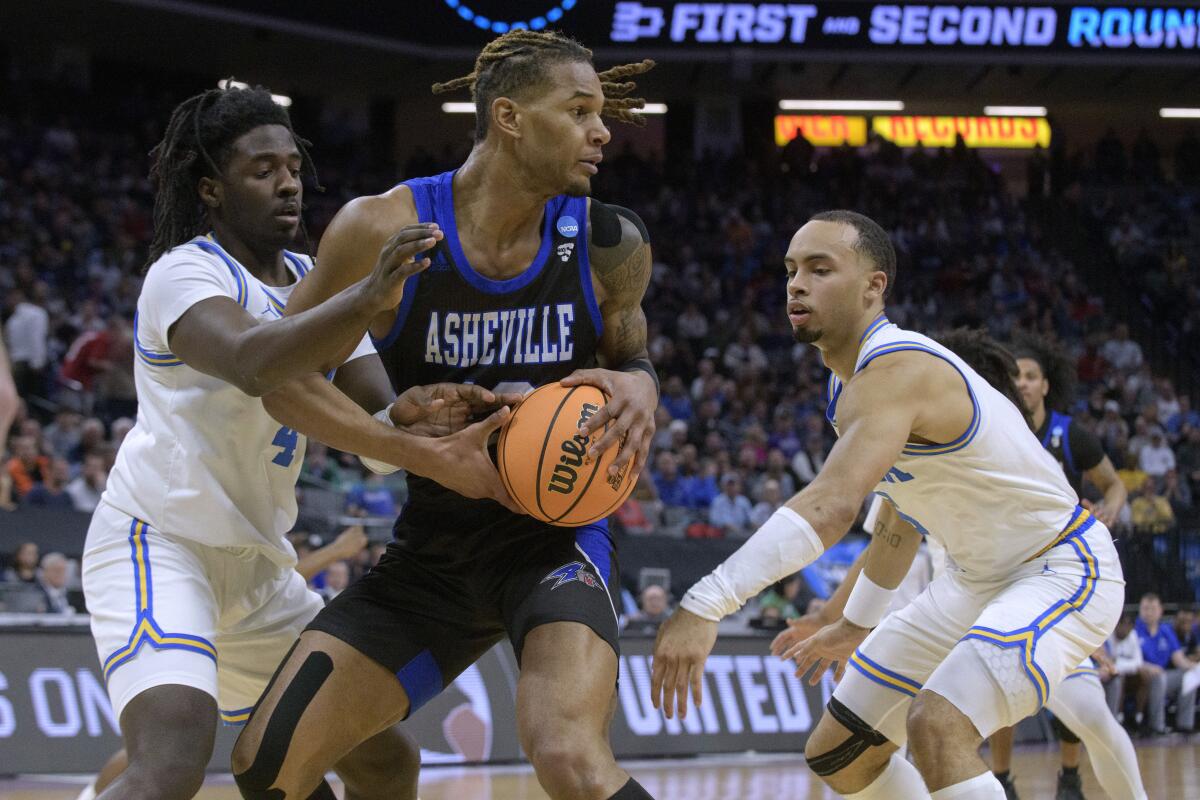 UNC Asheville forward Nicholas McMullen is guarded by UCLA guards Will McClendon and Amari Bailey.