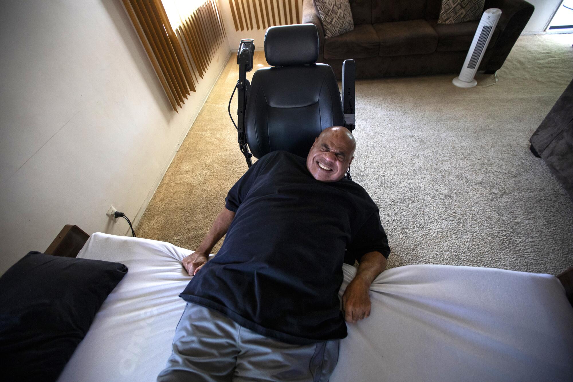 Bill Crawford pulls himself out of bed to his wheelchair in his living room 