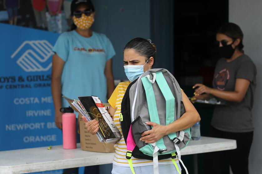 A local mom carries a new backpack for her son compliments of Newport-Balboa Rotary Club during distribution of back-to-school supplies at Rea Elementary School in Costa Mesa on Friday