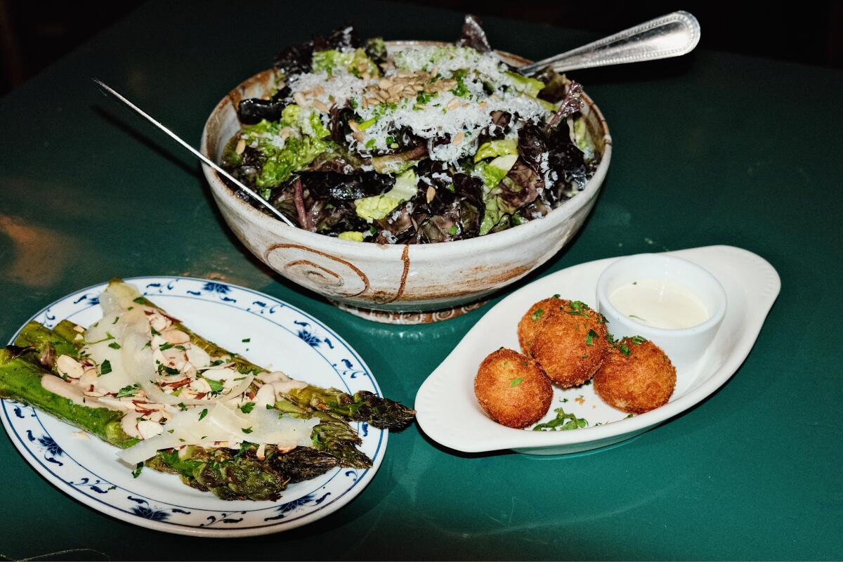 A plate of grilled asparagus, a large bowl of salad, and a small dish of fried bacalao on green tabletop at Cobras & Matadors
