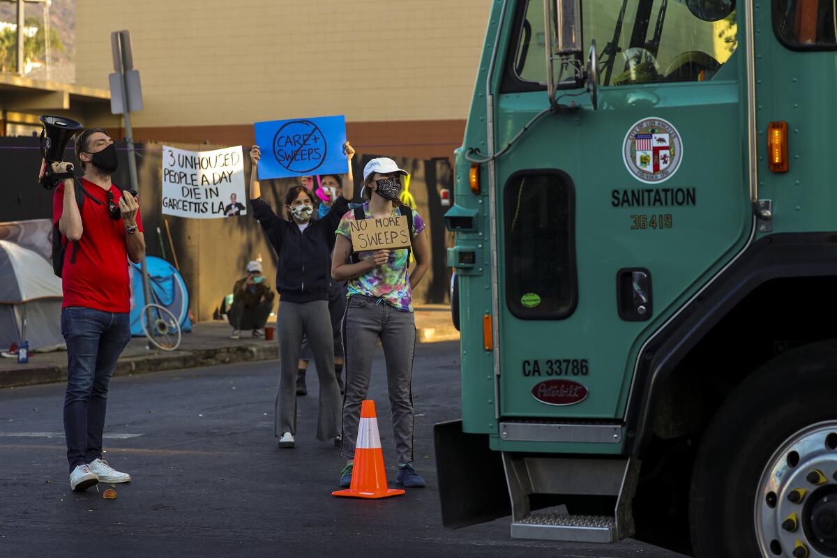 Protesters hold signs while standing in front of a green L.A. Sanitation Bureau truck on McCadden Place in Hollywood