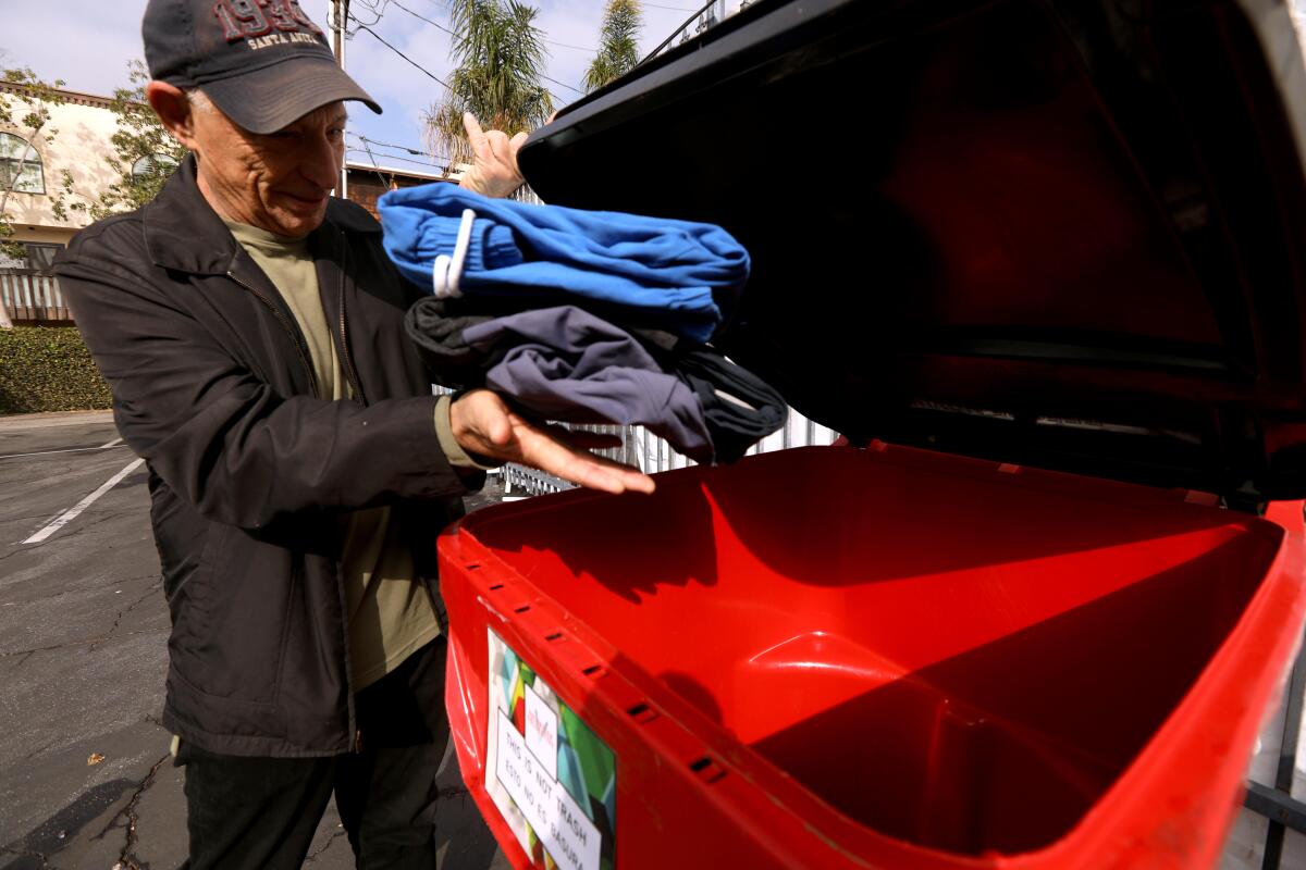 A man places a clothing donations in a red bin. 