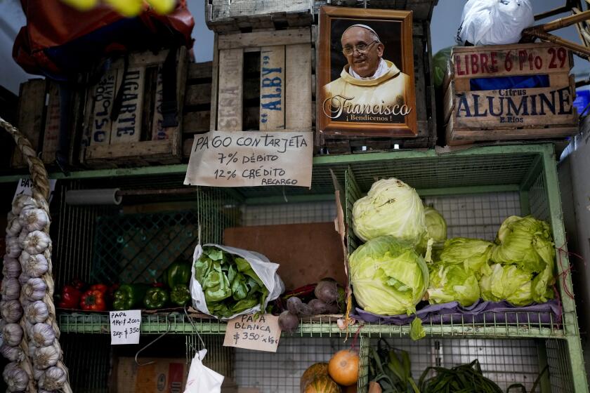 A picture of Pope Francis hangs beside a sign that reads in Spanish "With debit card 7%, with credit 12% increase," at a vegetable and fruit market in Buenos Aires, Argentina, Thursday, May 11, 2023. According to a recent World Bank Food Security report, Argentina has seen a 107% annual inflation rate in food prices. (AP Photo/Natacha Pisarenko)