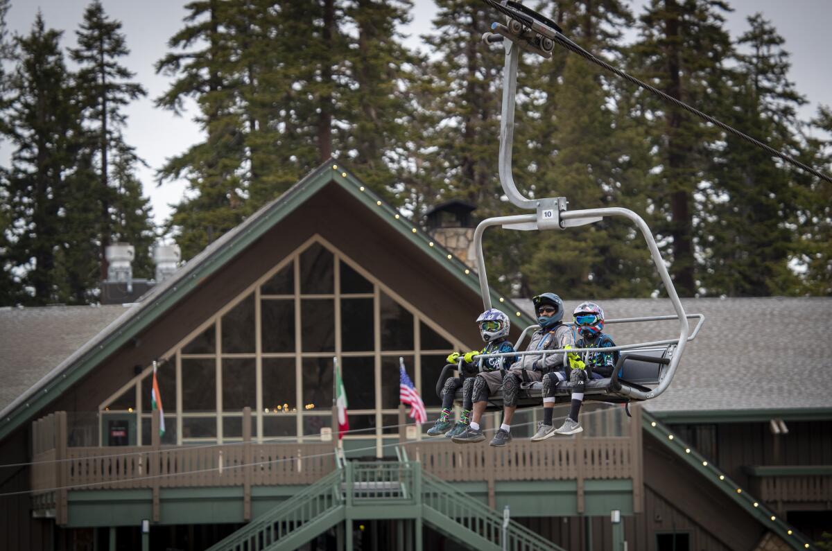 Three people in mountain biking gear take a chairlift to the top of a mountain.