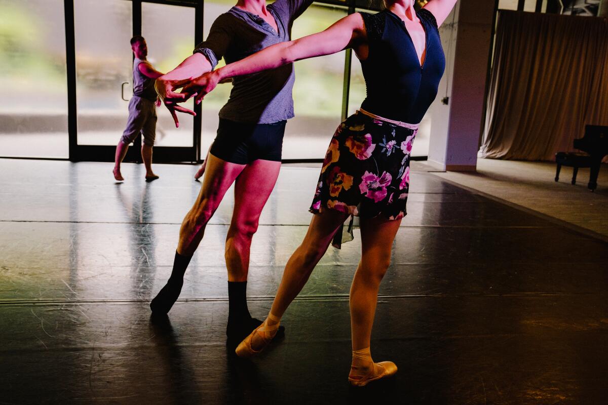 Dos bailarines con ropa de ensayo, vistos del cuello para abajo, en un estudio.