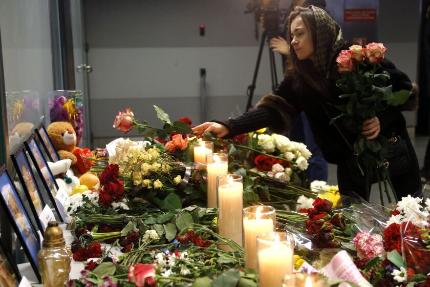 A woman lays flowers at a memorial of the flight crew members of the Ukrainian 737-800 plane that crashed on the outskirts of Tehran, at Borispil international airport outside in Kyiv, Ukraine, Saturday, Jan. 11, 2020. Ukraine's President Volodymyr Zelenskiy says that Iran must take further steps following its admission that one of its missiles shot down Ukrainian civilian airliner. (AP Photo/Efrem Lukatsky)