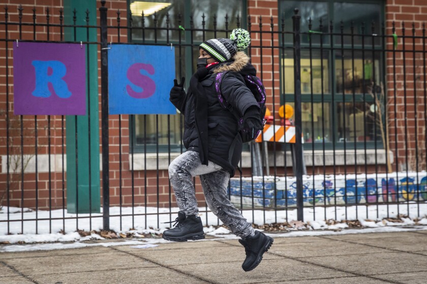 A student skips as they arrive at Jordan Community Public School in Rogers Park on the North Side, Wednesday, Jan. 12, 2022 in Chicago. Students returned to in-person learning Wednesday after a week away while the Chicago Public Schools district and the Chicago Teachers Union negotiated stronger COVID-19 protections. (Ashlee Rezin /Chicago Sun-Times via AP)