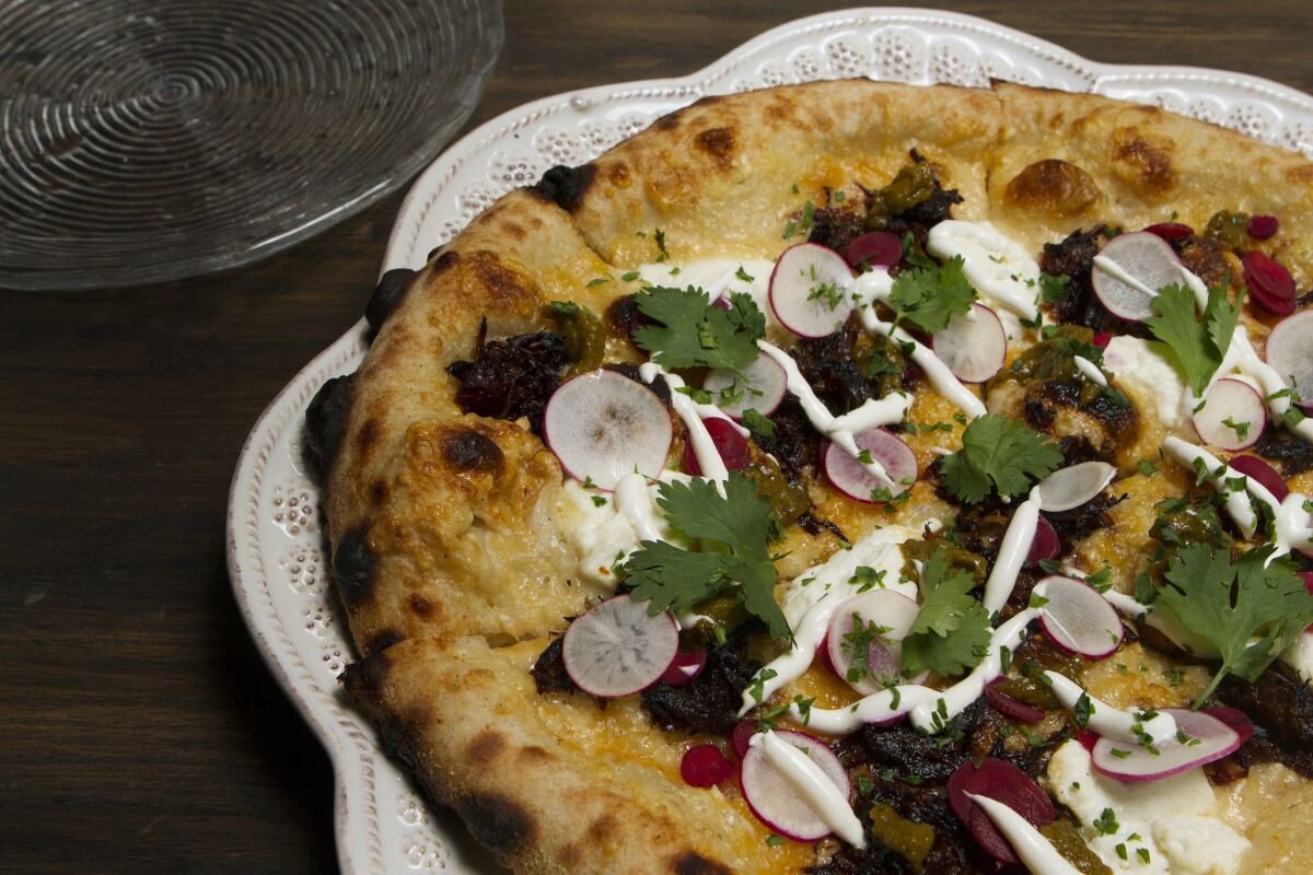 Carnitas pizza is made with confit pork, creme fraiche and chili verde. The tart salsa verde makes the pizza seem like an antojitos platform.