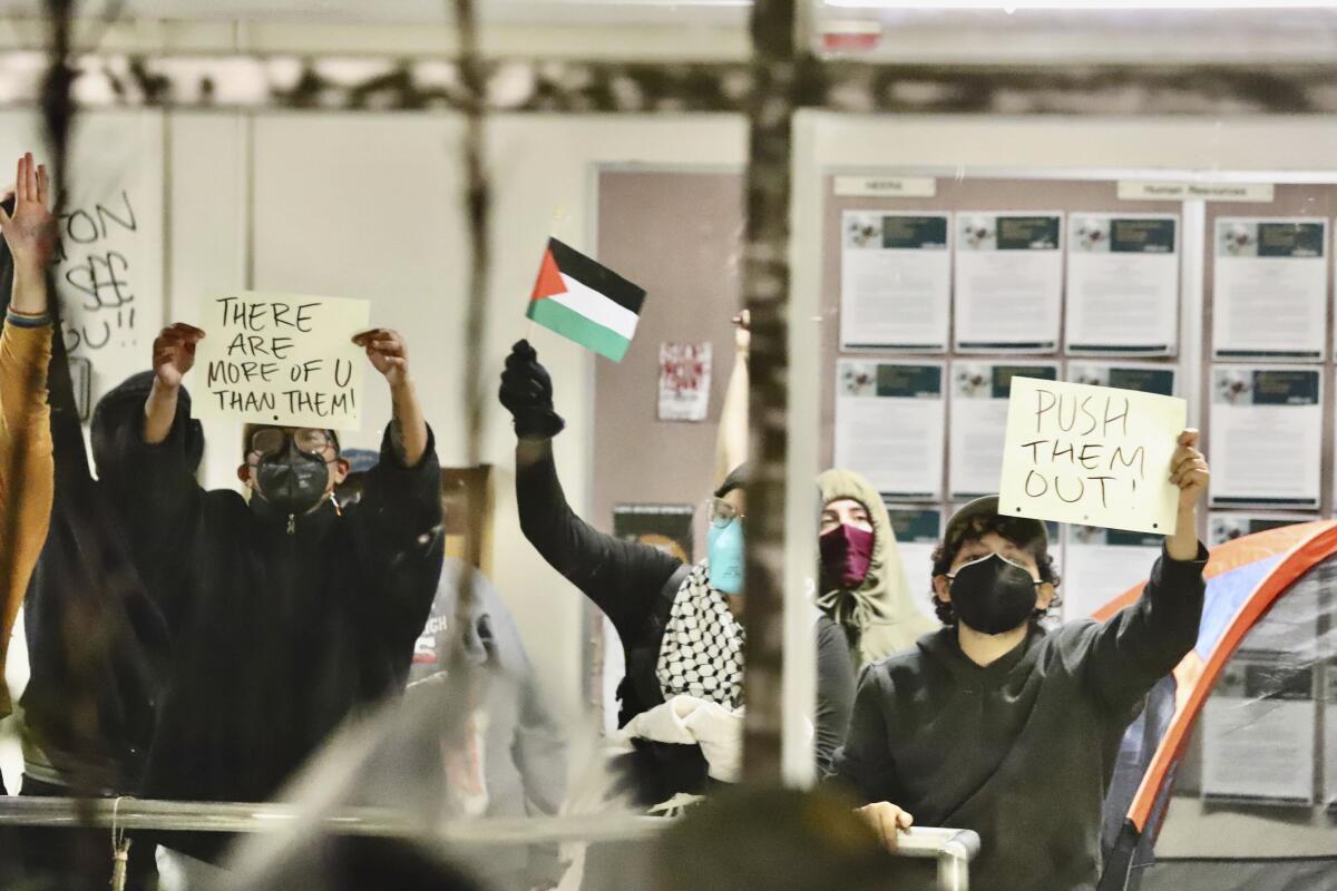 Masked protesters hold a Palestinian flag and signs including "Push Them Out."