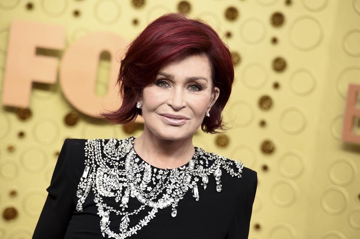 A woman with short red hair wearing a bejeweled black dress in front of a gold background