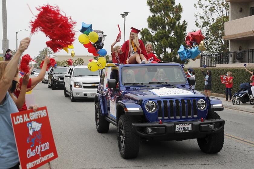 Graduate Kaylee Brown rides atop a jeep as she participates in a graduation car parade for Los Alamitos High School's Class of 2020 at The Shops At Rossmoor in Seal Beach on Wednesday morning.
