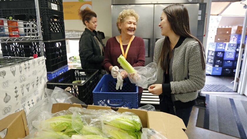 Cynthia Carson, center, chairwoman of operations for the Laguna Food Pantry board of directors, and volunteer Shikira Paul, right, separate bunches of romaine lettuce at the pantry on Tuesday.