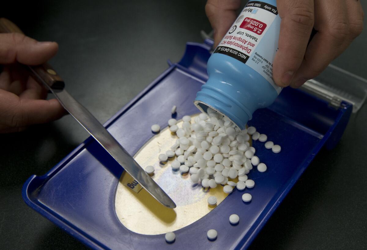 Dozens of pills are scooped into a bottle by a person holding a knifelike tool. 
