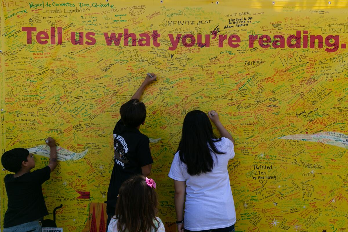 People write on a wall that says, "Tell us what you're reading."