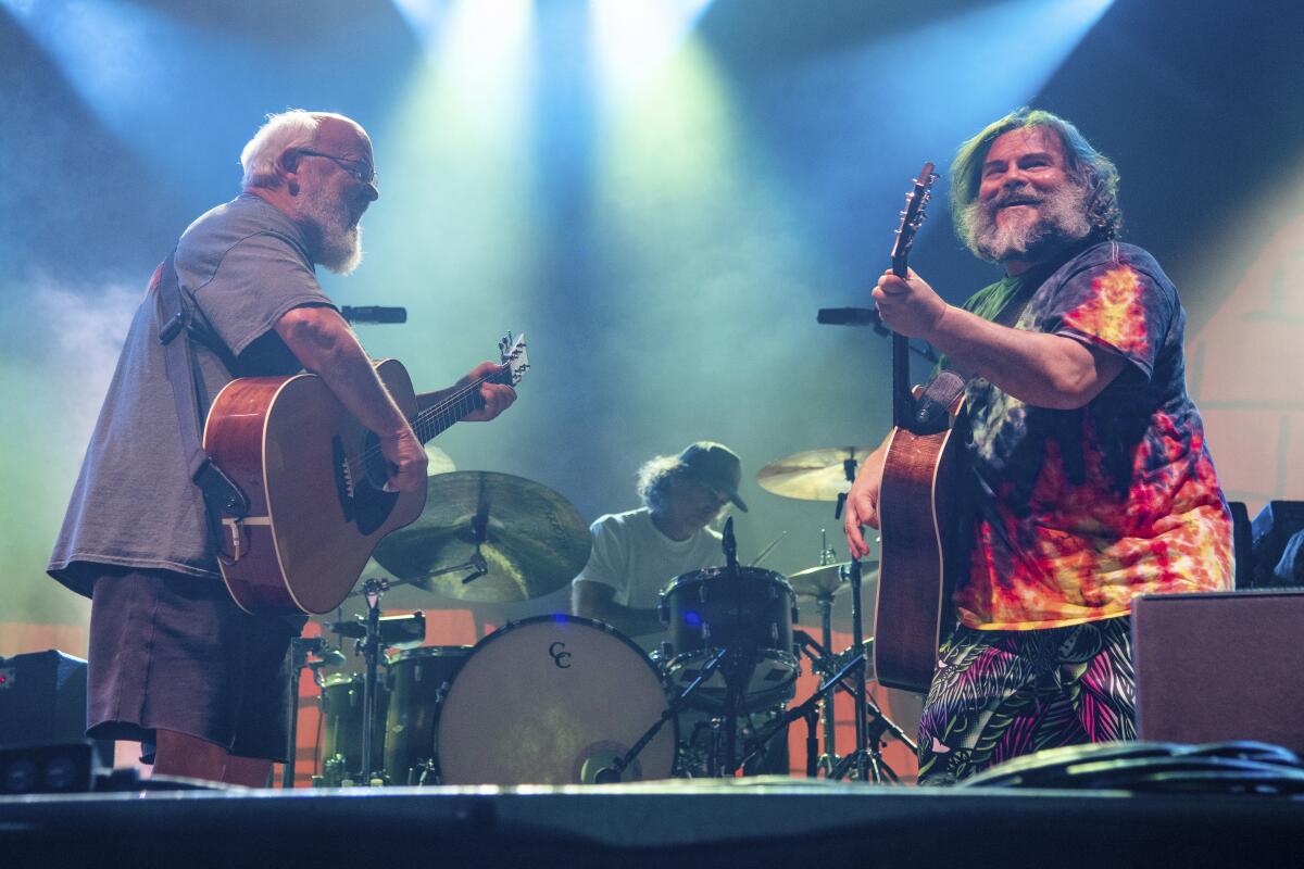 Kyle Gass and Jack Black play guitars onstage in front of a man playing a drumkit