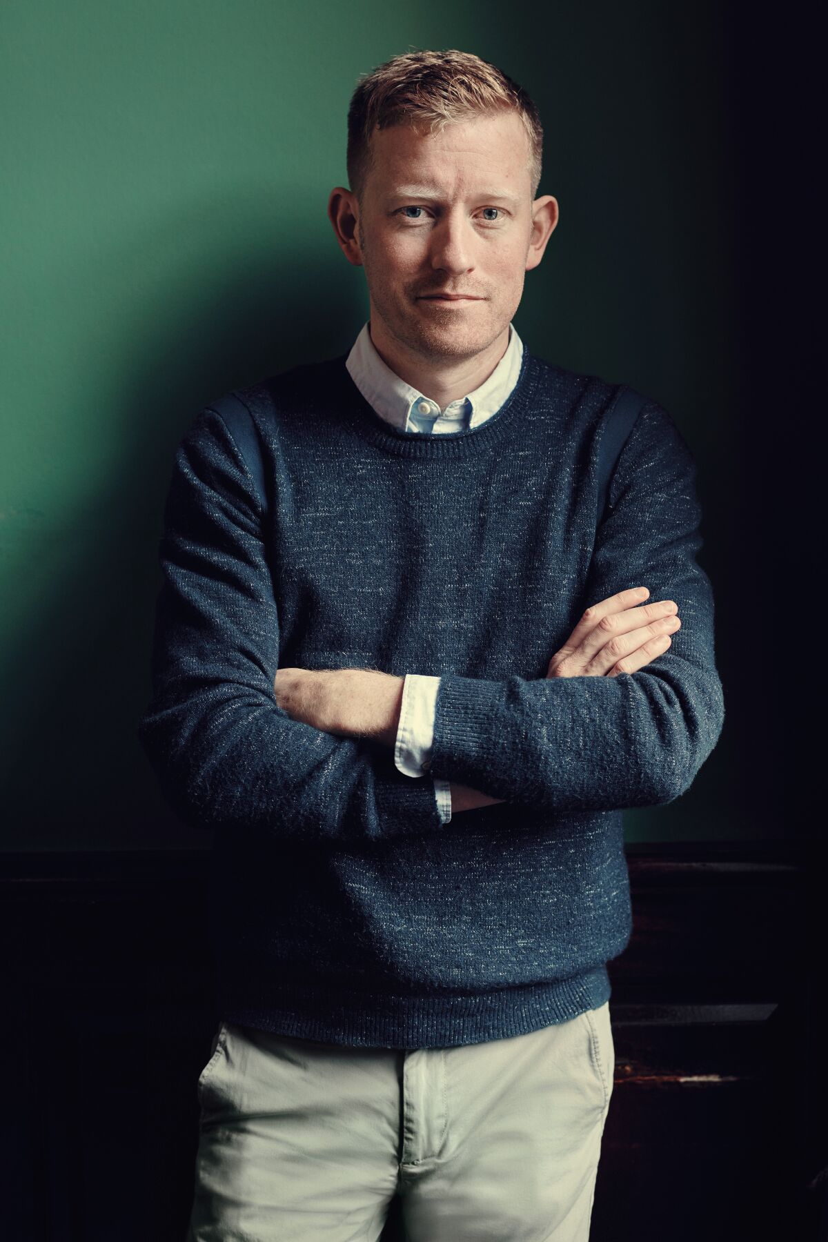 A man in a navy blue sweater folds his arms.