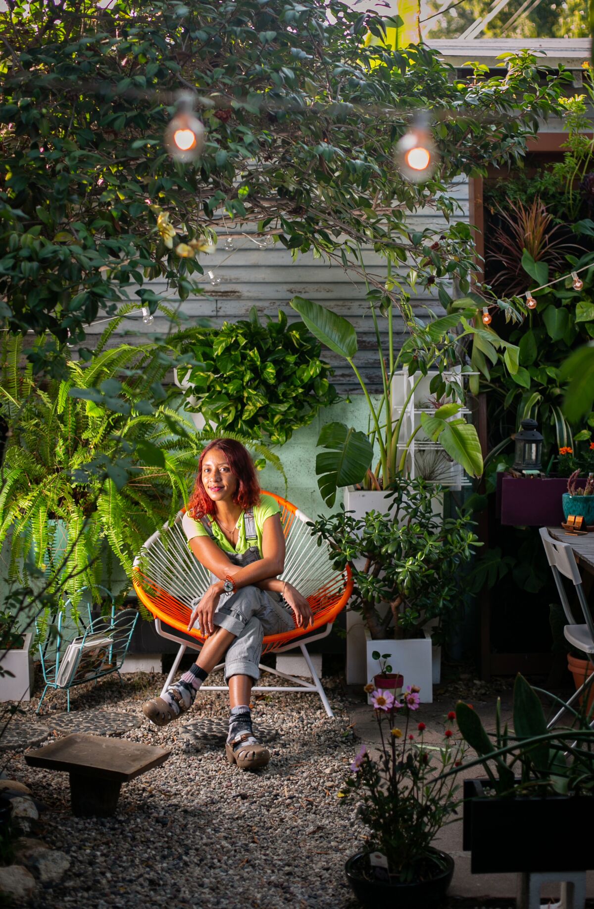 A woman sits in an orange Modern chair surrounded by plants