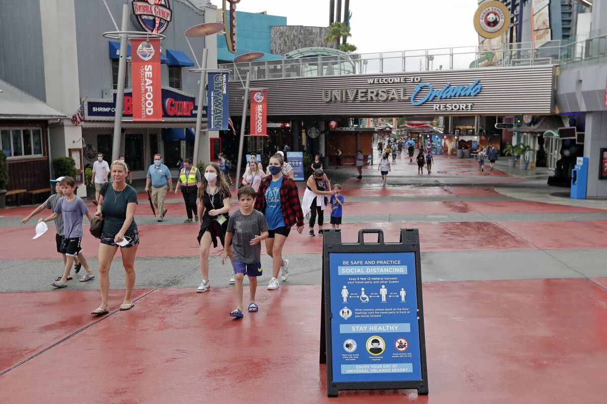 FILE - Signs about social distancing and other protocols are seen about the theme park as guests walk by at Universal Orlando Resort Wednesday, June 3, 2020, in Orlando, Fla. Company officials said Wednesday, Jan. 12, 2022 that workers at Universal’s theme parks must be fully vaccinated by Feb. 9 or be required to take a test every week. (AP Photo/John Raoux, File)