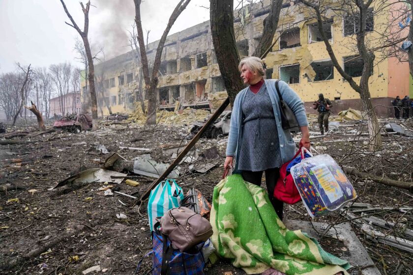 A woman walks outside the damaged by shelling maternity hospital in Mariupol, Ukraine, Wednesday, March 9, 2022. 