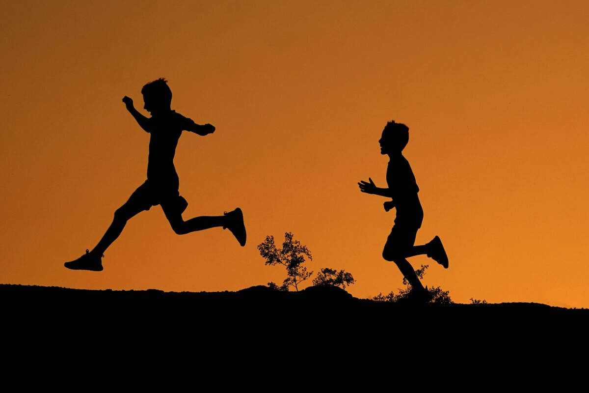 Boys are silhouetted against the sky at sunset as they run along a ridge at Papago Park, Friday, April 1, 2022, in Phoenix. (AP Photo/Charlie Riedel)