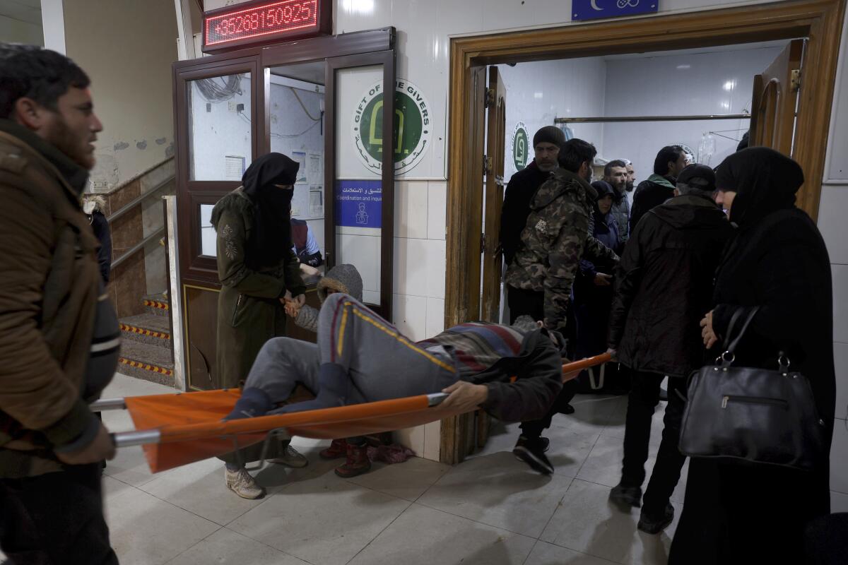 A person on a stretcher is carried toward a doorway where other people are standing 