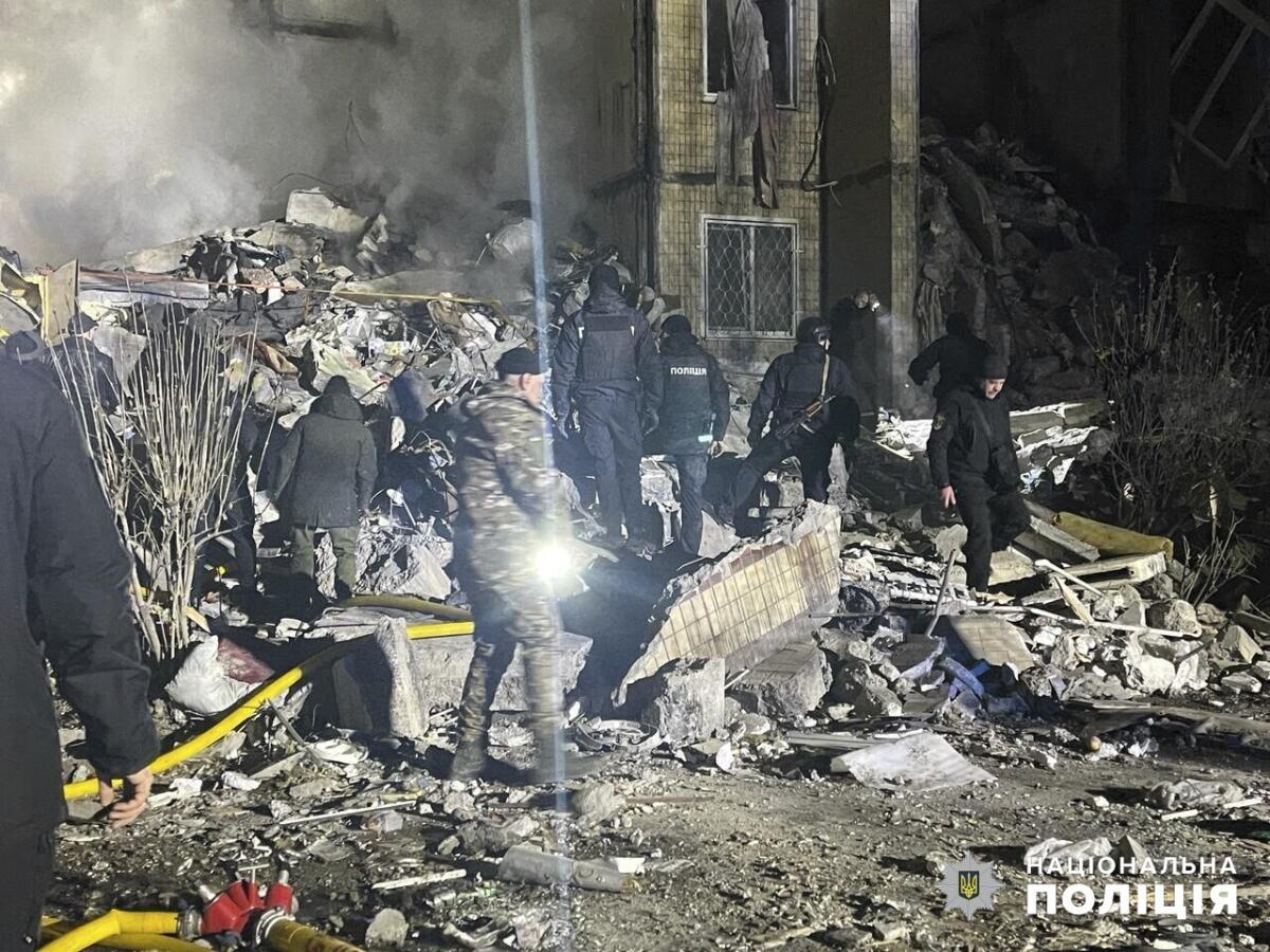 People with hoses and flashlights work next to rubble at night.