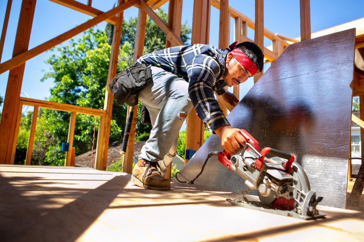 A worker surrounded by construction framing cuts plywood