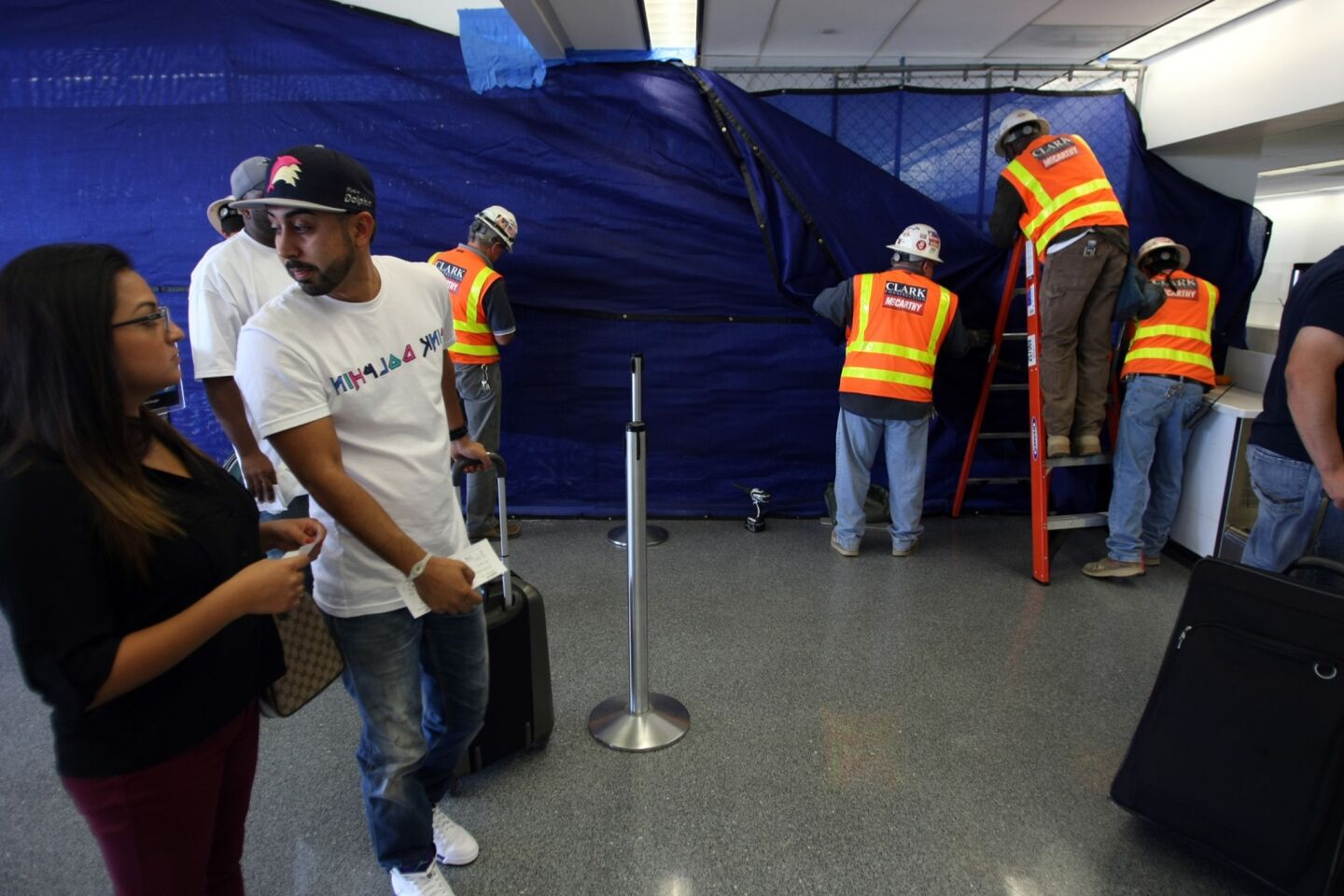 Travelers wait to check in as construction workers take down tarp that prevented people from looking at the crime scene.